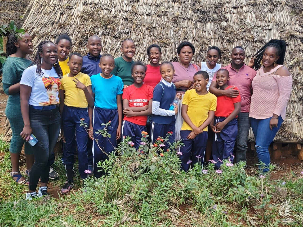 Smiling pupils and teachers outside a thatched hut during a community visit