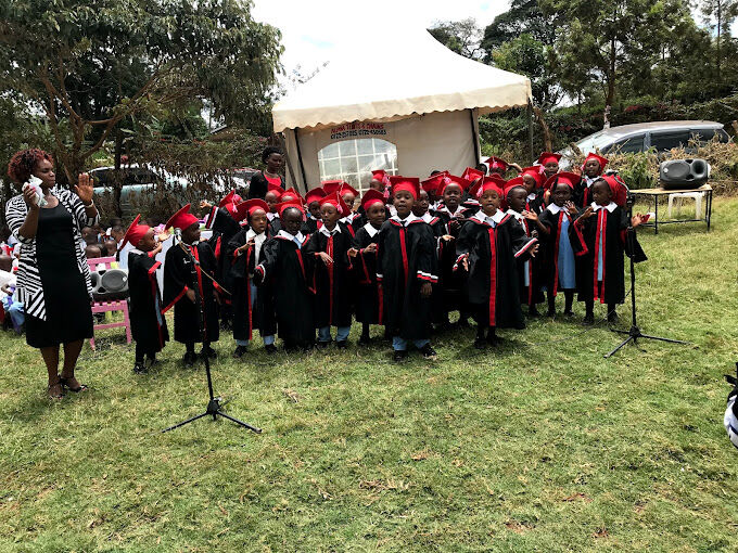 Pupils in red graduation caps and black gowns singing at the graduation ceremony