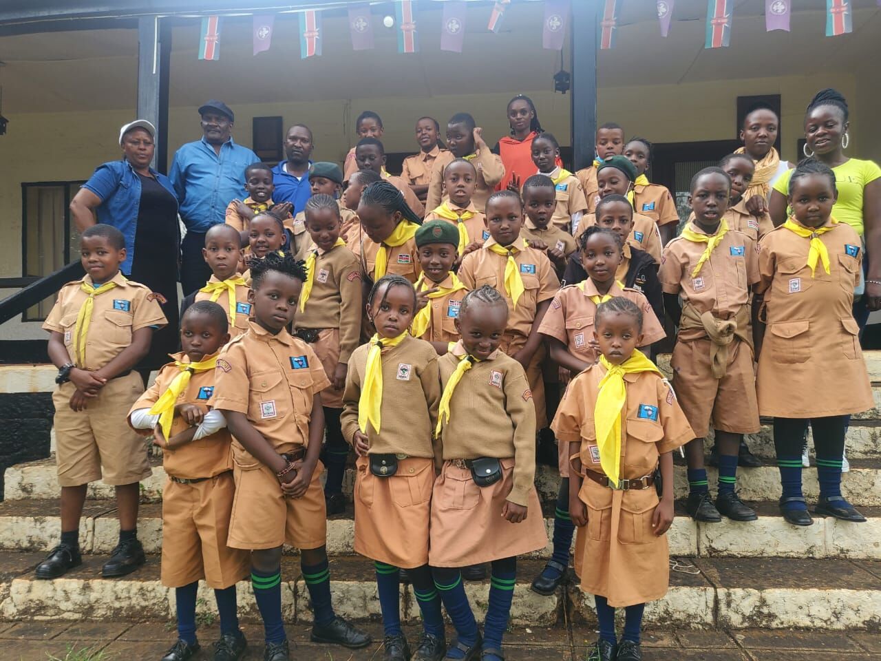 Scouts and guides in uniform with yellow scarves on the steps of a building