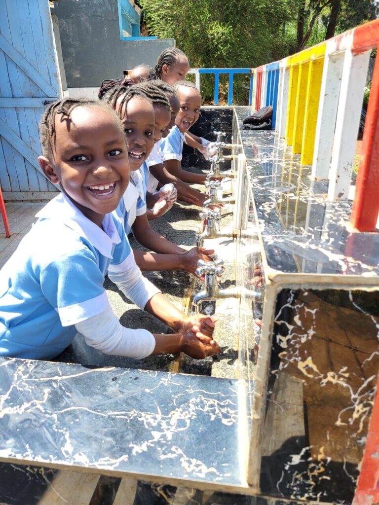 A smiling pupil in a sky-blue uniform washing hands at the school handwashing station