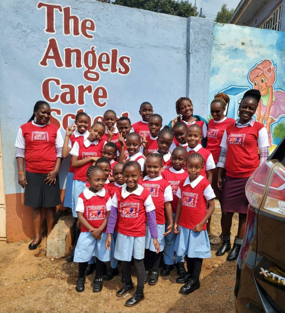 Pupils and teachers in red T-shirts smiling in front of the painted school wall